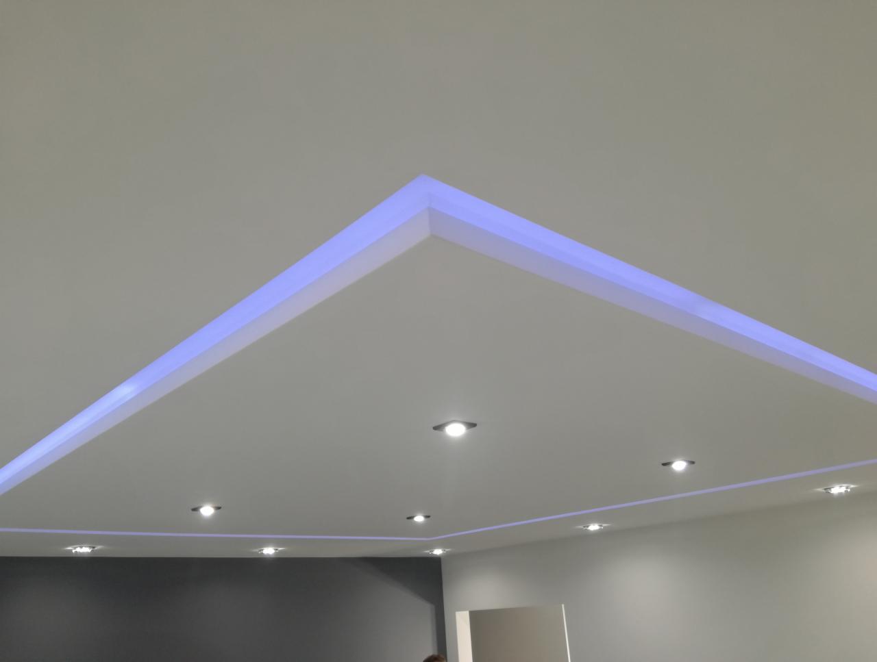 Nowoczesny sufit z podświetleniem LED w kolorze niebieskim, w kształcie geometrycznym, z zamontowanymi punktowymi lampami halogenowymi.