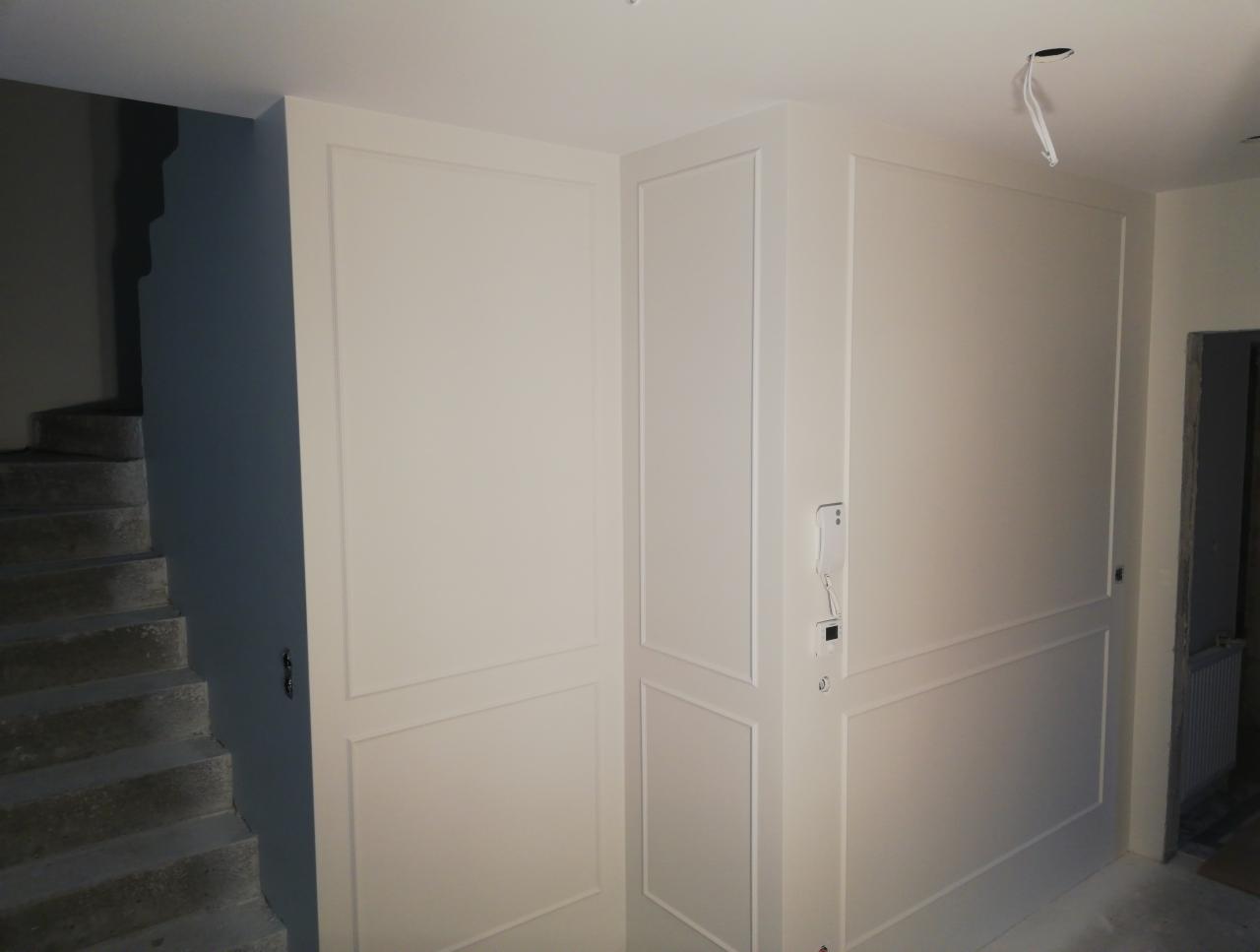 Wykończone wnętrze: białe ściany z dekoracyjnymi listwami, szare betonowe schody, widoczny interkom.