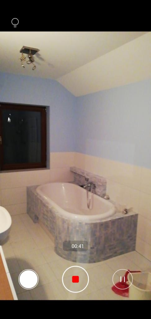 Niedawno wyremontowana łazienka z wanną obudowaną mozaiką, ściany pomalowane częściowo na biało i niebiesko, widoczne ślady po pracy, nagranie z telefonu.