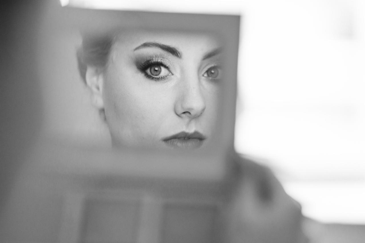 Czarno-białe zbliżenie twarzy panny młodej w Katowicach, odbijającej się w lustrze, z wyraźnym makijażem oczu, wykonane podczas reportażu ślubnego.