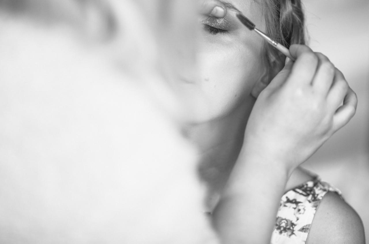 Czarno-białe zbliżenie twarzy kobiety podczas wykonywania makijażu brwi pędzelkiem, widoczny delikatny makijaż oka.