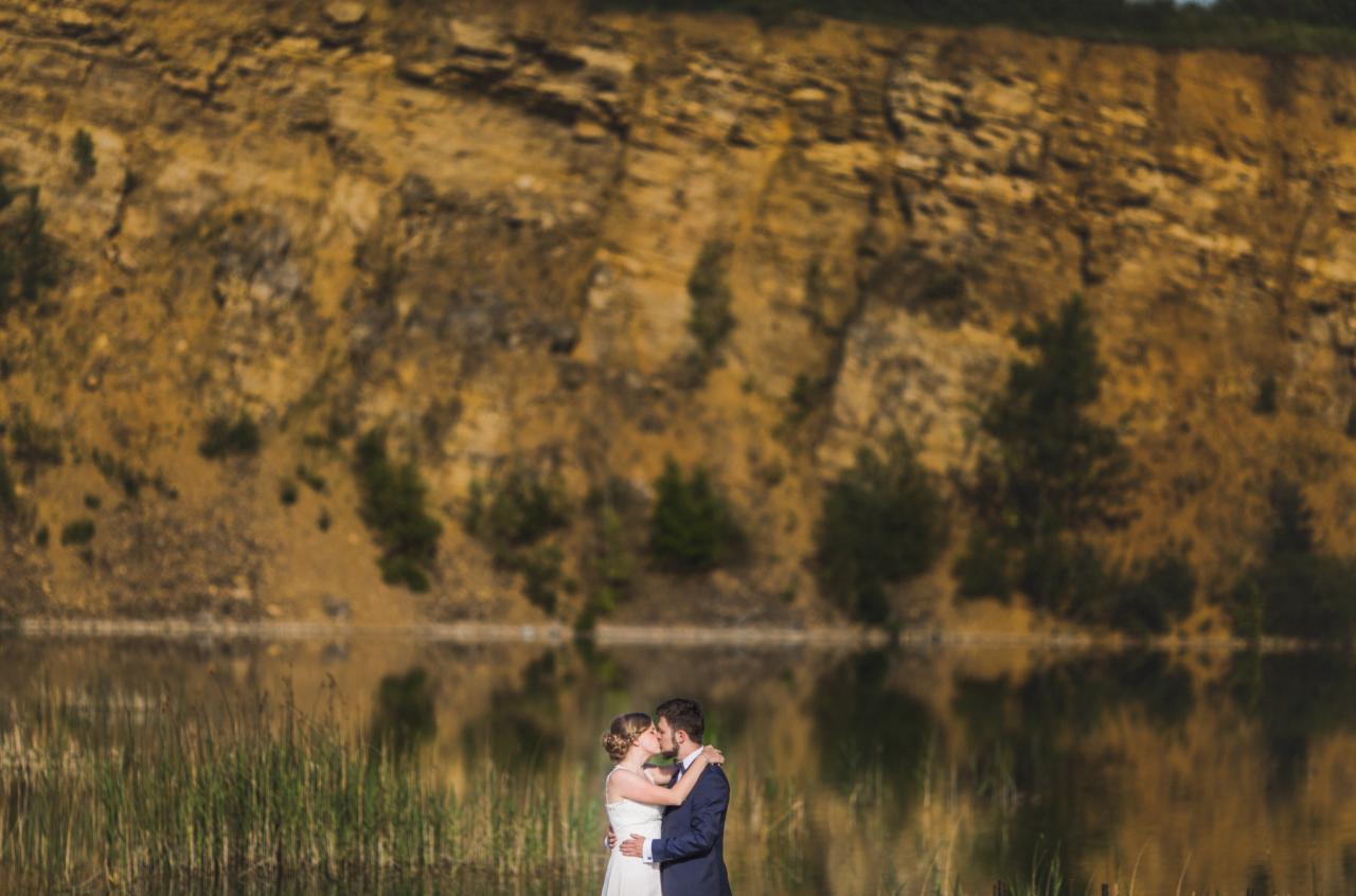 Para młoda całuje się na tle skalnego krajobrazu i jeziora w plenerze ślubnym.