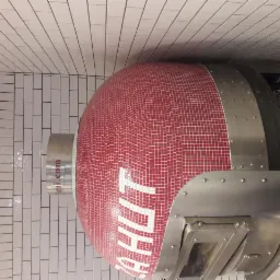 Piec do pizzy z czerwoną mozaiką i napisem, otoczony białymi, podłużnymi płytkami na ścianie i suficie.