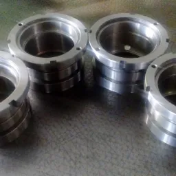 Cztery metalowe, pierścieniowe elementy z otworami i wycięciami, ułożone w dwóch stosach na szarej powierzchni, wykonane techniką obróbki CNC.