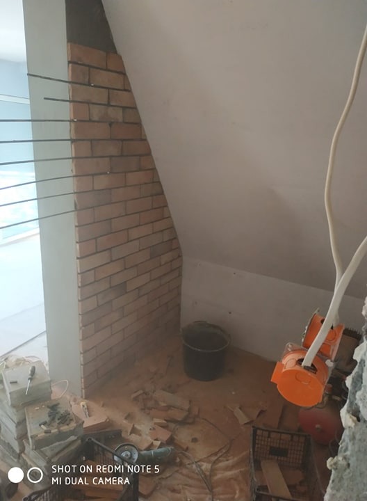 Montaż cegieł dekoracyjnych na ścianie pod skosem poddasza, widoczne narzędzia glazurnicze i resztki materiałów.