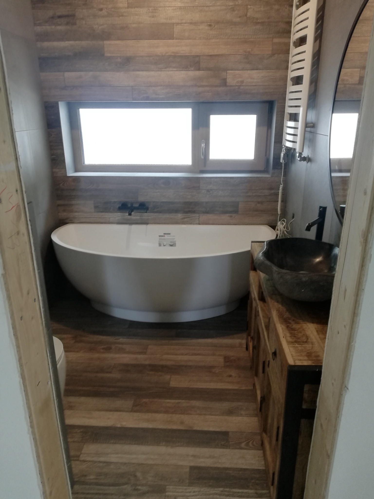 Nowoczesna łazienka w Przełęku z wolnostojącą wanną, umywalką w stylu kamiennym na drewnianej szafce i grzejnikiem drabinkowym na ścianie wyłożonej płytkami imitującymi drewno.