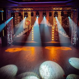 TWENTY ONE- Profesjonalna Obsługa Muzyczna- Jarosław Sitarz - Scena z oświetleniem scenicznym: reflektory punktowe tworzą okrągłe plamy światła na parkiecie, w tle dekoracja z połyskujących elementów i schody.