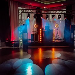 TWENTY ONE- Profesjonalna Obsługa Muzyczna- Jarosław Sitarz - Scena z oświetleniem scenicznym, reflektory, kratownica i kolumny głośnikowe, przygotowana do występu, z elementami dekoracyjnymi w tle.