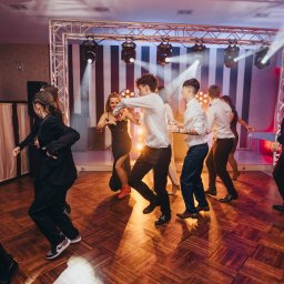 TWENTY ONE- Profesjonalna Obsługa Muzyczna- Jarosław Sitarz - Grupa osób tańczy na parkiecie podczas imprezy, oświetlenie sceniczne z tyłu, parkiet z drewnianych klepek, ujęcie z perspektywy parkietu.
