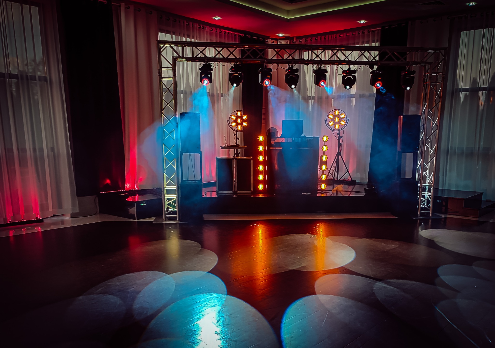 Scena z oświetleniem scenicznym, reflektory, kratownica i kolumny głośnikowe, przygotowana do występu, z elementami dekoracyjnymi w tle.