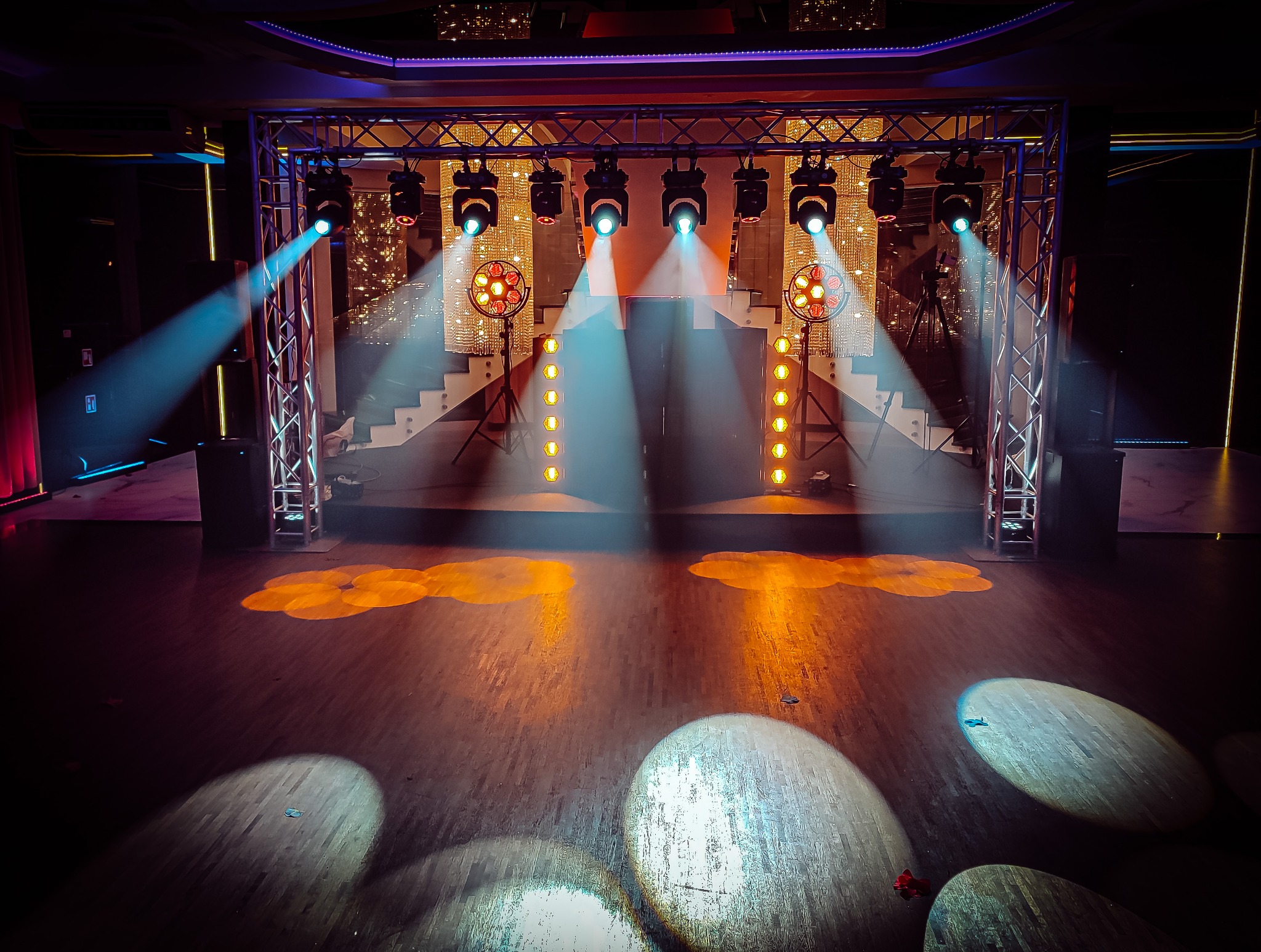 Pusta scena oświetlona reflektorami, z metalową konstrukcją oświetleniową, schodami w tle i wzorami świetlnymi na podłodze.