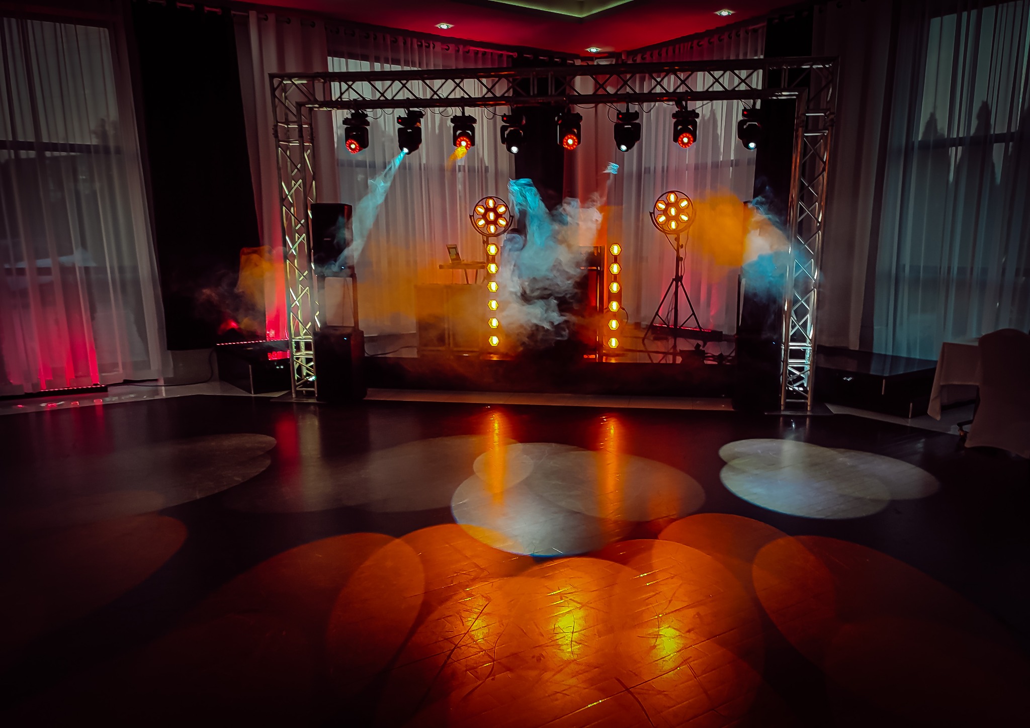 Scena z oświetleniem eventowym: reflektory, dym, konstrukcja kratowa, światła punktowe na podłodze.