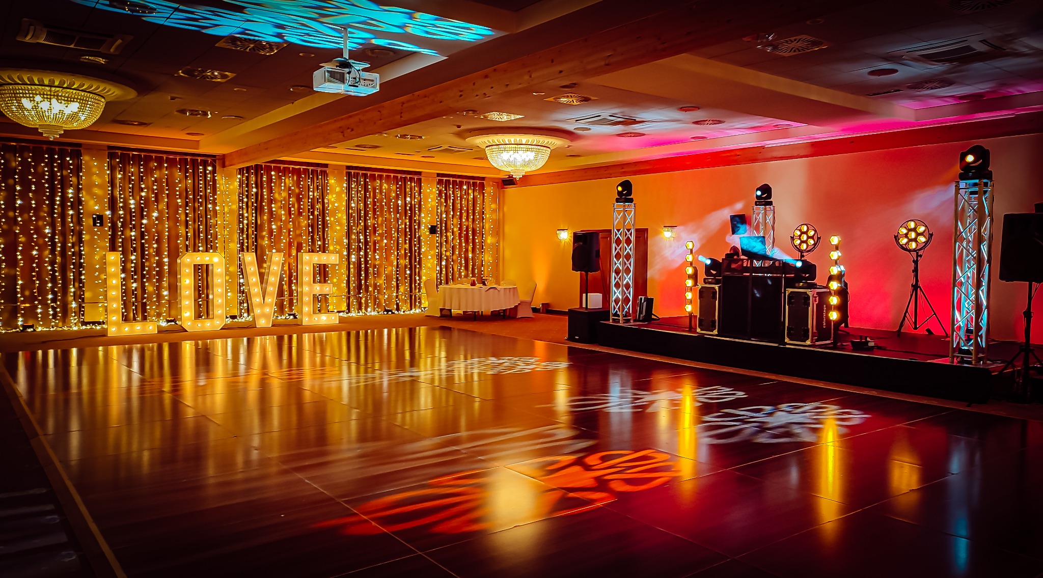 Sala balowa z parkietem odbijającym światła, scena z konsoletą DJ-a i oświetleniem, dekoracja świetlna w postaci napisu LOVE oraz kurtyny z lampek.