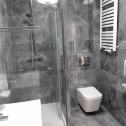 Nowoczesna łazienka z kabiną prysznicową typu walk-in, wiszącą toaletą i grzejnikiem drabinkowym na tle ścian wyłożonych płytkami imitującymi marmur w odcieniach szarości.