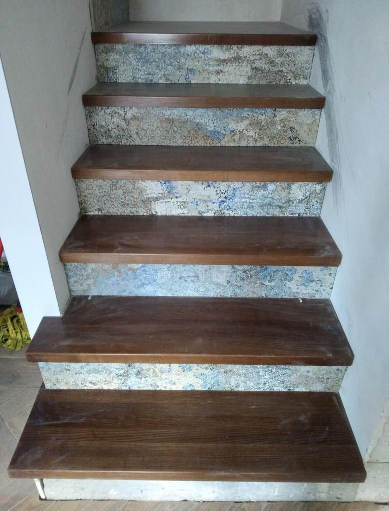 Schody z drewnianymi stopniami i wzorzystymi podstopnicami w trakcie prac wykończeniowych, widoczne niedociągnięcia na ścianie i podłodze.