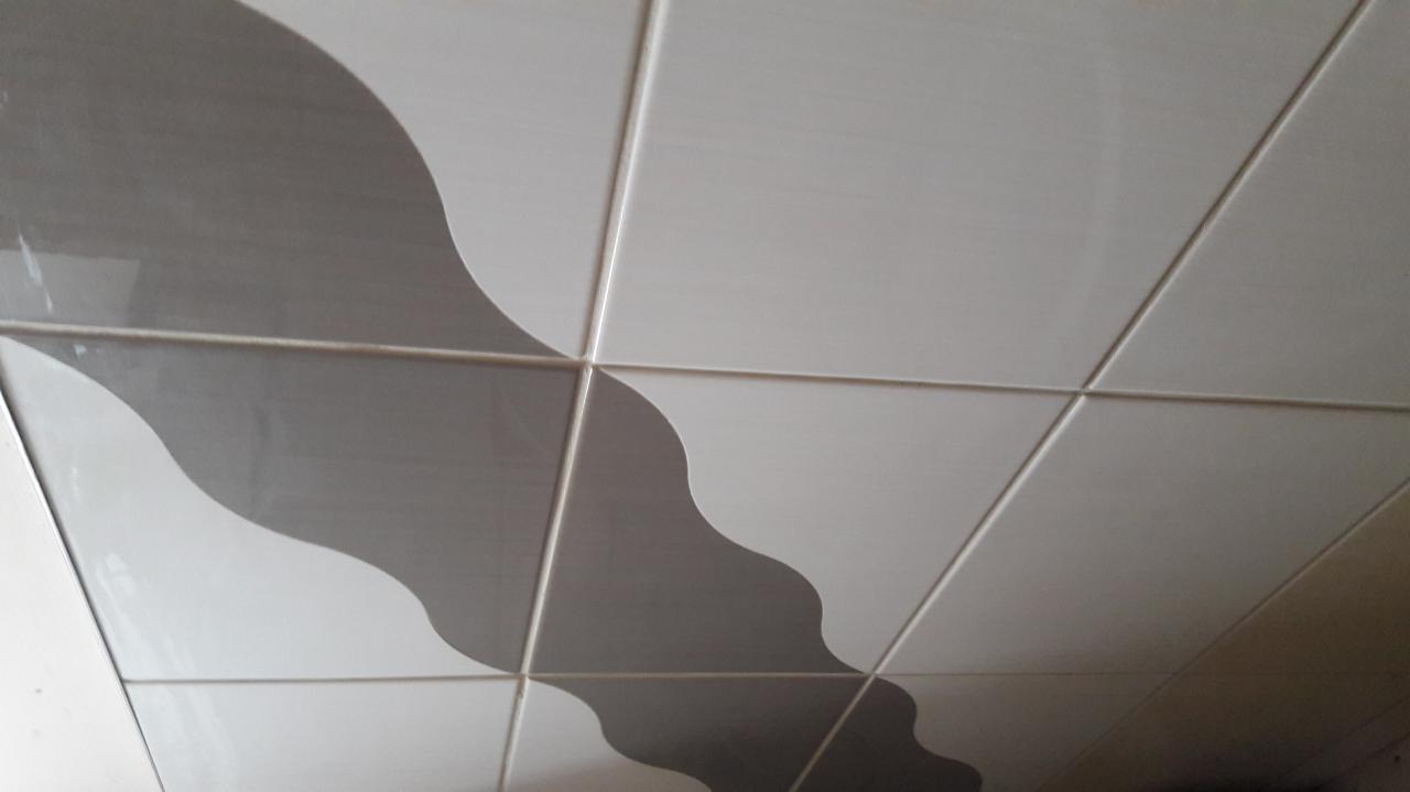 Świeżo położone, błyszczące, kwadratowe płytki ceramiczne w odcieniach szarości i bieli, ułożone ukośnie, tworzące falisty wzór na ścianie.