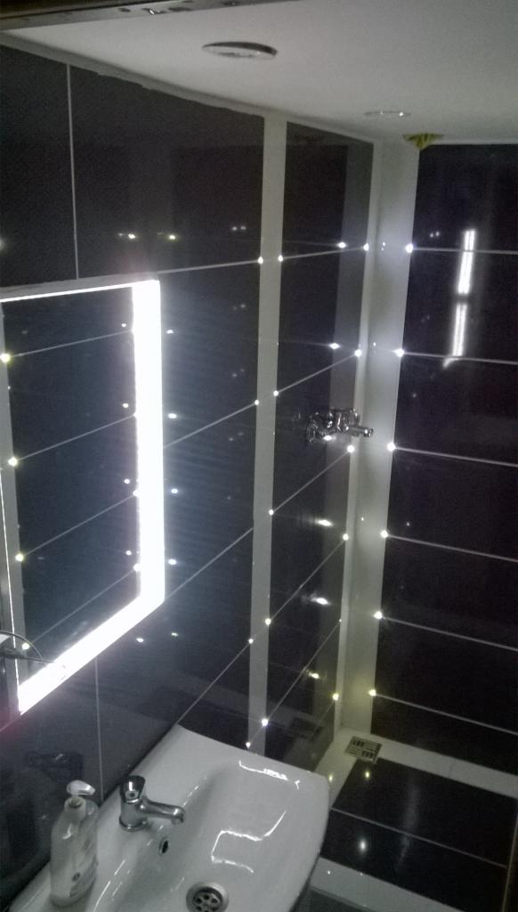 Wykończona łazienka z czarnymi płytkami i białymi fugami, umywalka narożna, bateria jednouchwytowa, oświetlenie punktowe w fugach.