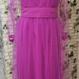 Manekin prezentuje fuksjową sukienkę z tiulowymi rękawami i ozdobnym paskiem, na tle ściany z motywem bluszczu.