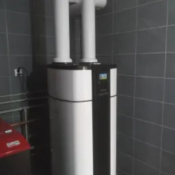 Biało-czarny piec kondensacyjny marki Gabriel Spectra z dwoma białymi kominami, zainstalowany w pomieszczeniu z szarymi płytkami w Wąsoszu.