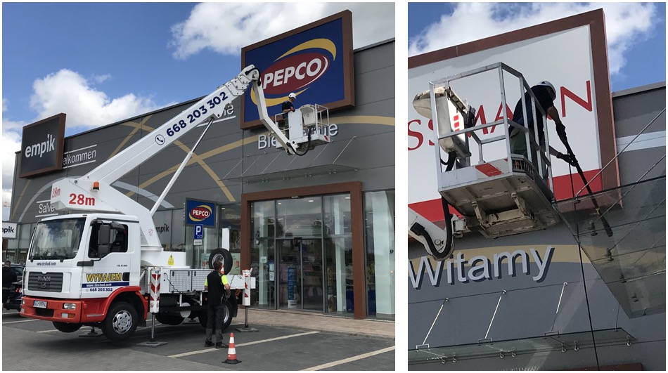 Pracownik na podnośniku koszowym czyści elewację sklepu Pepco, widoczny również sklep Empik i zaparkowany samochód ciężarowy.