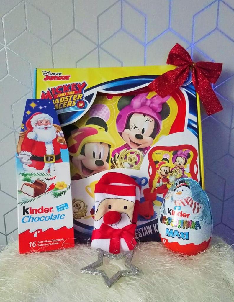 Zestaw upominkowy dla dziecka z motywem Myszki Miki, zawierający słodycze Kinder, pluszową ozdobę w kształcie Świętego Mikołaja oraz srebrną gwiazdkę na puszystym tle.