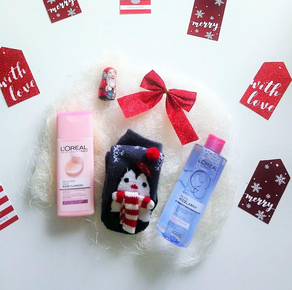 Kosmetyki L'Oreal, skarpetka z pingwinem i ozdoby świąteczne na białym, puszystym tle, tworzące kompozycję prezentową.