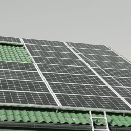 Panele słoneczne na zielonym dachu z dachówki ceramicznej, widoczny komin i drabina oparta o dach.