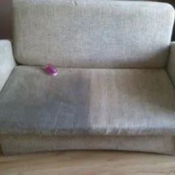 Dwukolorowa kanapa po częściowym praniu, widoczna różnica między wyczyszczoną a brudną powierzchnią, na oparciu leży fioletowa gumka do włosów.