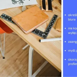 Jasny drewniany biurko z pomarańczowym krzesłem, skórzanym notesem z wytłoczonym logo, czarnym kątownikiem, białym markerem i kartką z napisem, całość w naturalnym oświetleniu.