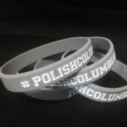 Trzy szare silikonowe bransoletki z wytłoczonym białym napisem '#POLISHCOLUMBIA' ułożone na czarnym tle.
