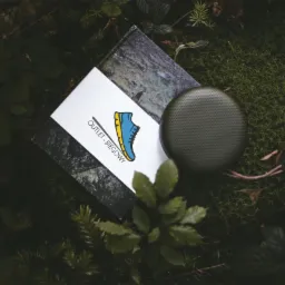 Pudełko z logo sklepu biegowego i głośnik na mchu w leśnym otoczeniu.