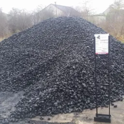 Góra czarnego węgla kamiennego na placu składowym, obok tabliczka informacyjna z ceną 780 zł.