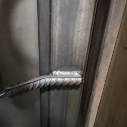 Spoina łącząca żebrowany pręt z metalowym profilem, widoczne niedoskonałości spoiny i zabrudzenia na metalu.