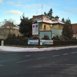 Siedziba firmy z tablicą informacyjną na rogu ulicy, częściowo pokryta śniegiem, w tle budynek biurowy i zaparkowany van.