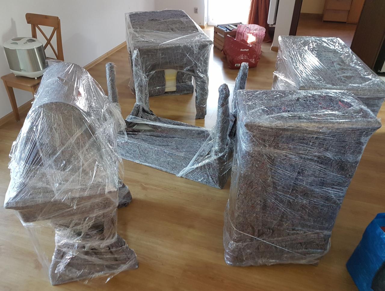 Meble zabezpieczone folią i kocami transportowymi podczas przygotowań do przewozu, widoczne krzesła, stół oraz kartony w tle.