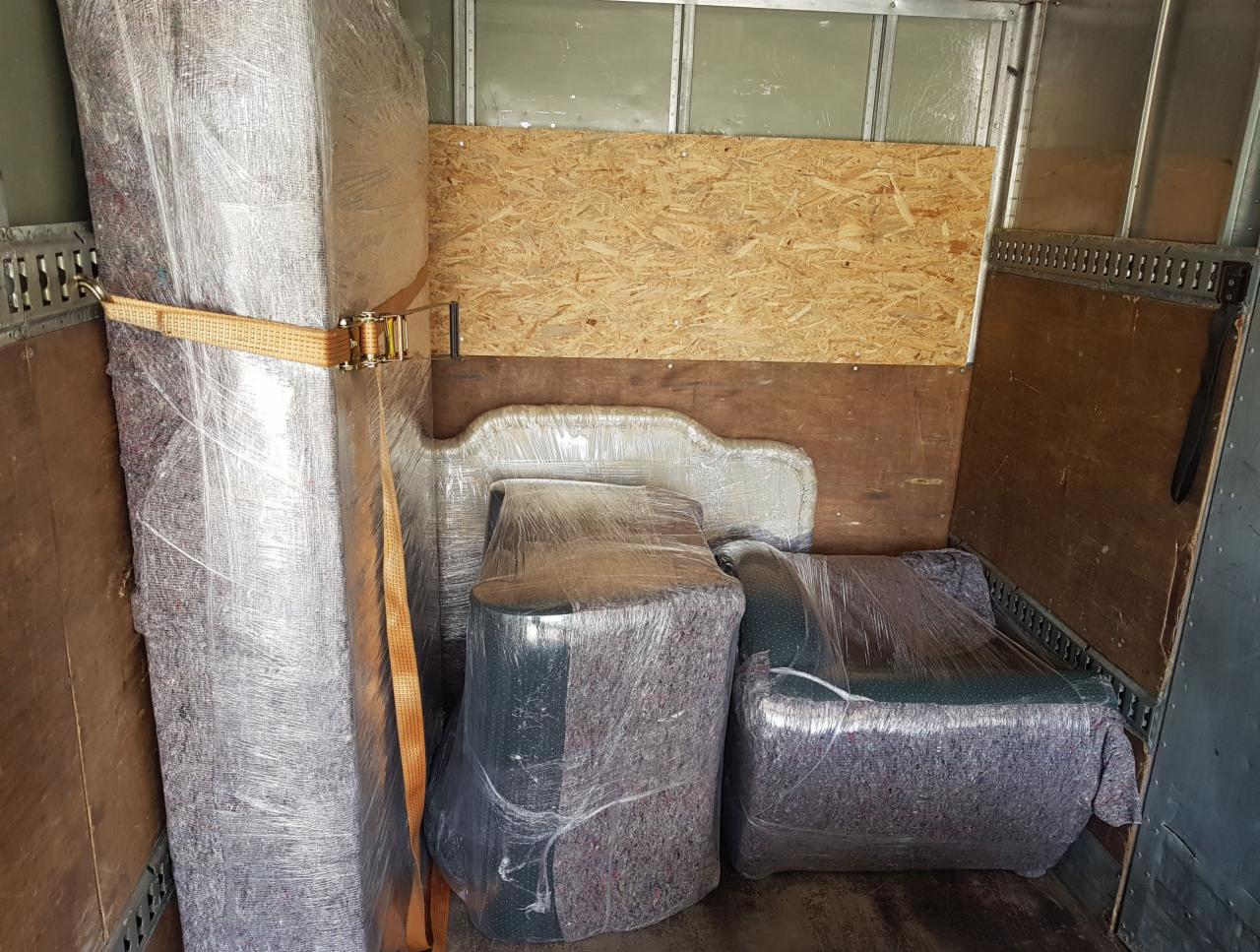 Wnętrze furgonetki wypełnione meblami zabezpieczonymi folią stretch i pasami transportowymi, gotowymi do przewozu.