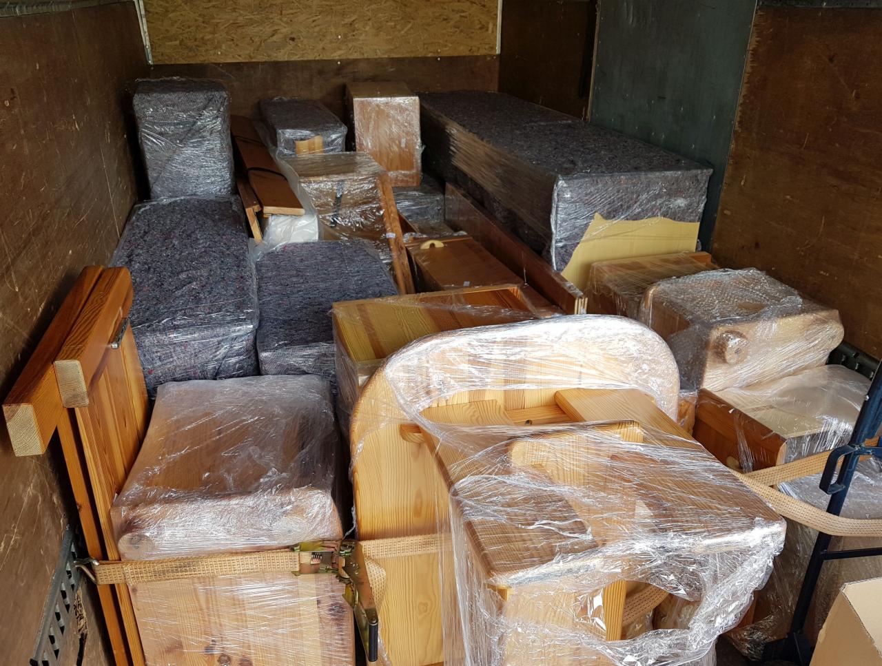 Wnętrze skrzyni ładunkowej wypełnionej meblami zabezpieczonymi folią i kocami, gotowymi do transportu.