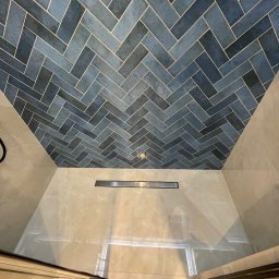 Your modern house - Niebieska mozaika ułożona w jodełkę na suficie kabiny prysznicowej, widoczny odpływ liniowy i fragment szklanej ściany kabiny.