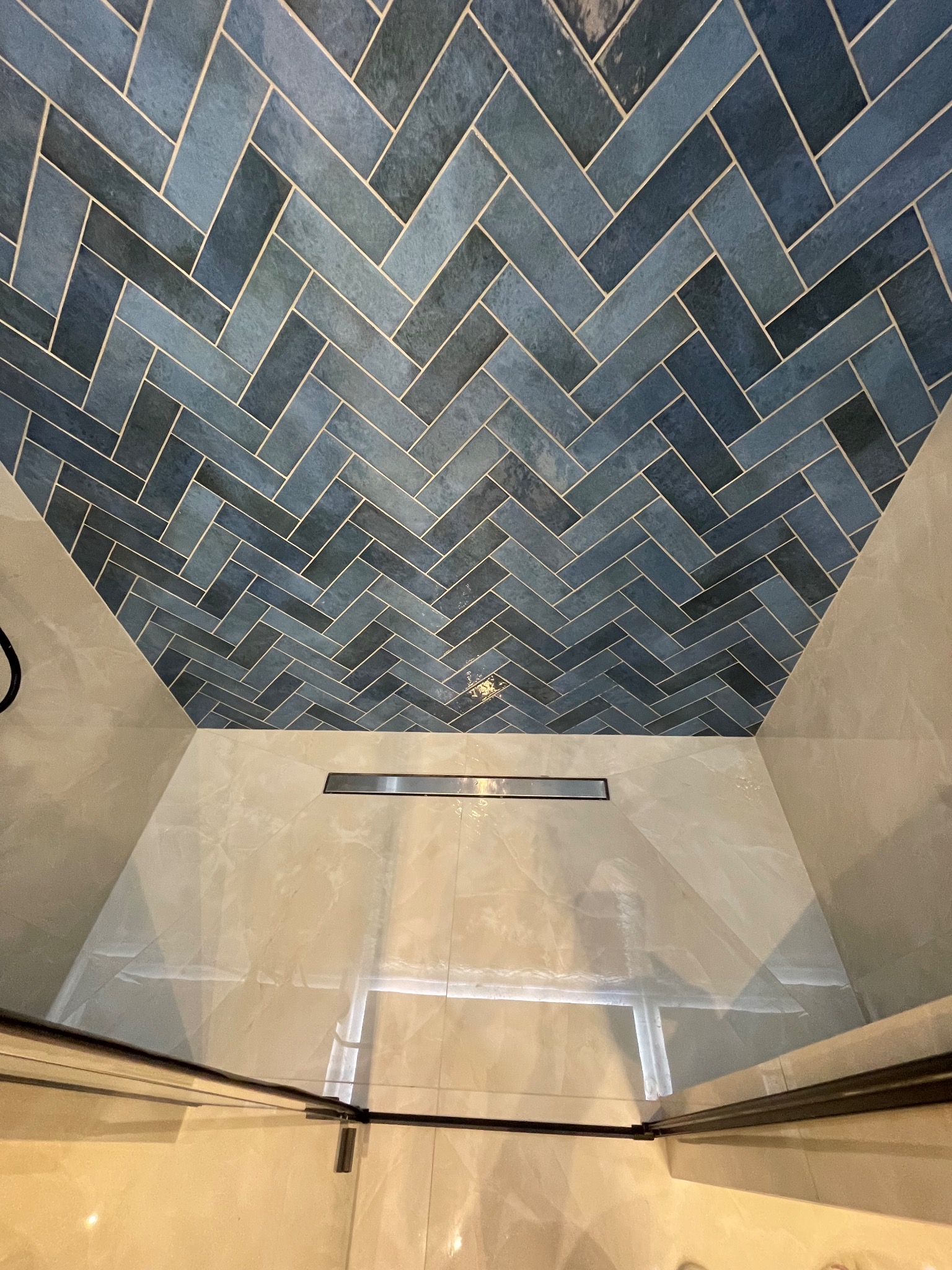 Niebieska mozaika ułożona w jodełkę na suficie kabiny prysznicowej, widoczny odpływ liniowy i fragment szklanej ściany kabiny.