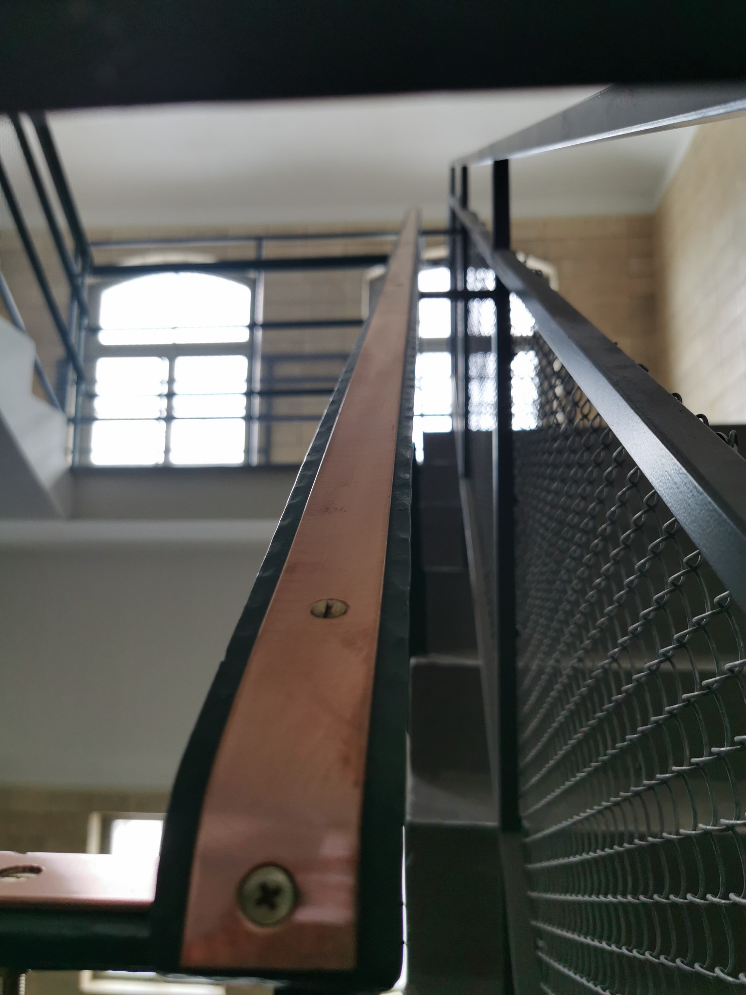Metalowa balustrada schodowa z miedzianym wykończeniem poręczy, widok z dołu na okno.