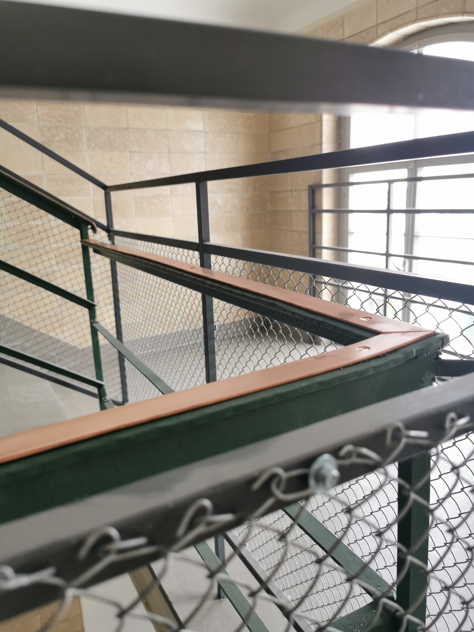 Metalowa konstrukcja klatki schodowej z siatką zabezpieczającą, widok z dołu, elementy pomalowane na zielono i brązowo.