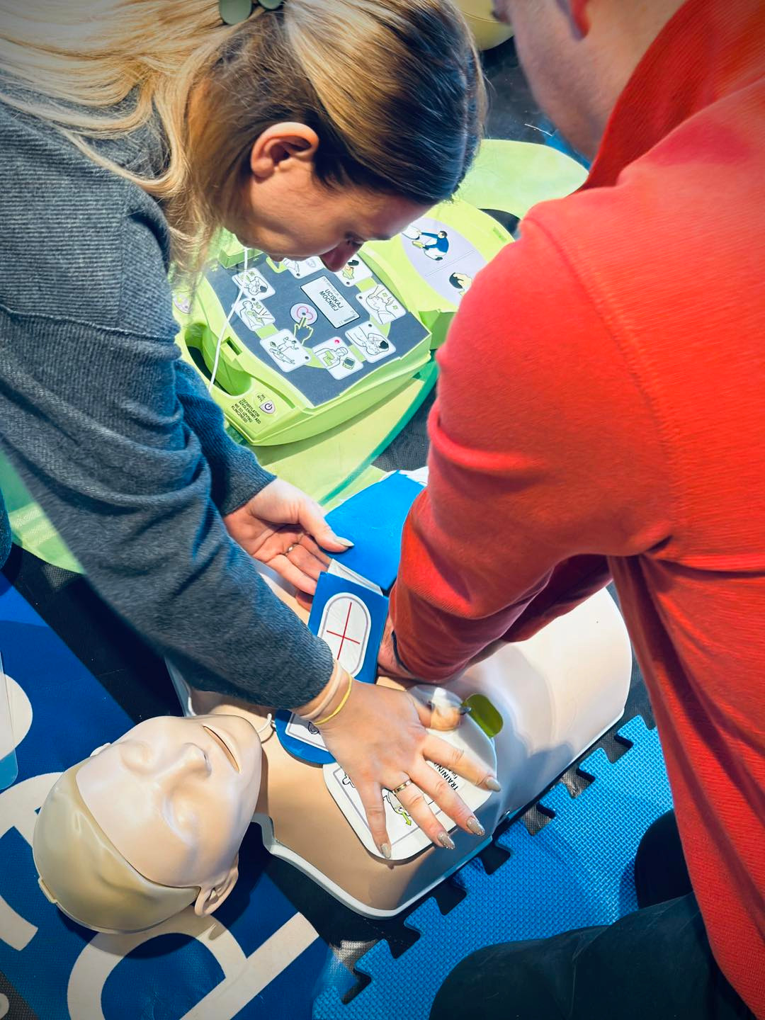 Instruktorzy demonstrują użycie defibrylatora AED i masaż serca na fantomie podczas zajęć praktycznych.