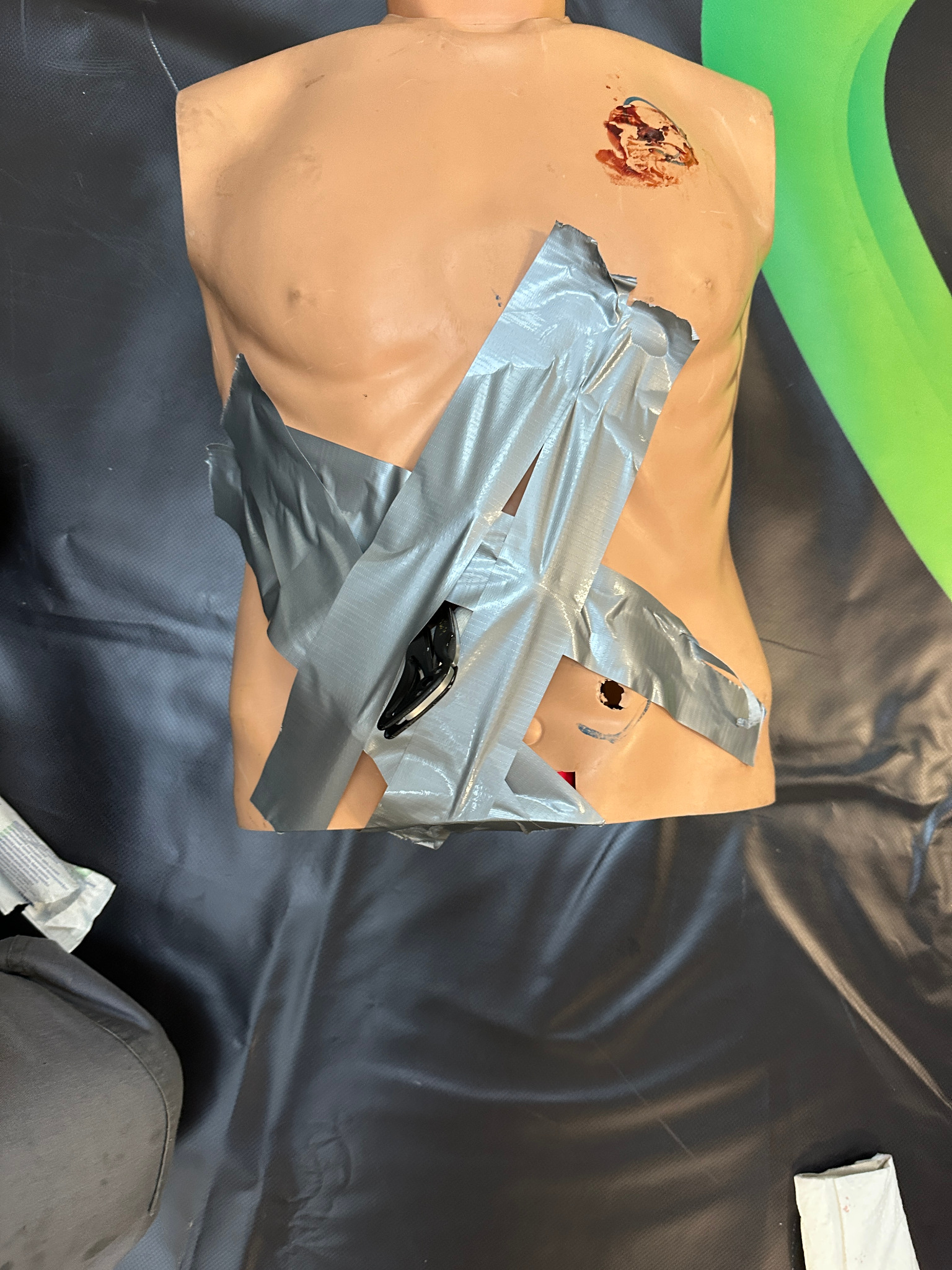 Manekin treningowy z ranami na torsie, zabezpieczonymi szarą taśmą klejącą.