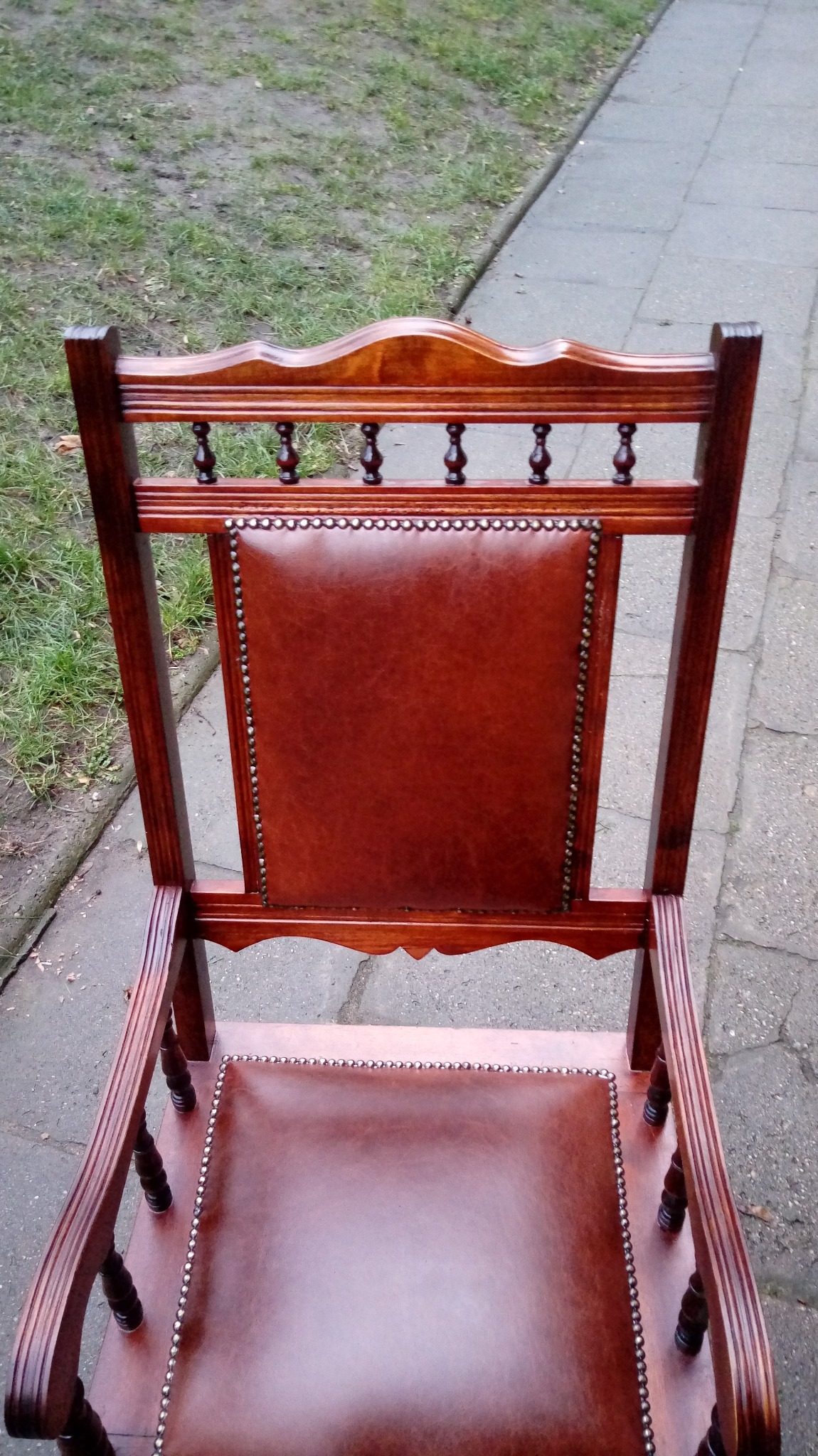 Widok z góry na odnowiony, ciemnobrązowy fotel z brązową skórzaną tapicerką, zdobioną nitami, stojący na zewnątrz na betonowym chodniku.