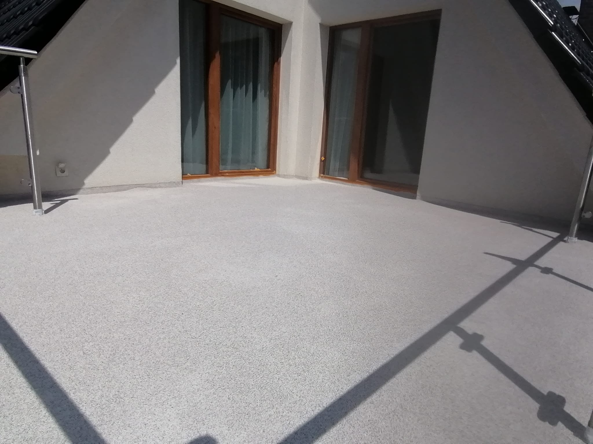 Balkon z nową, jasnoszarą posadzką żywiczną o drobnej fakturze, widoczne drewniane ramy okienne i fragment metalowej balustrady.
