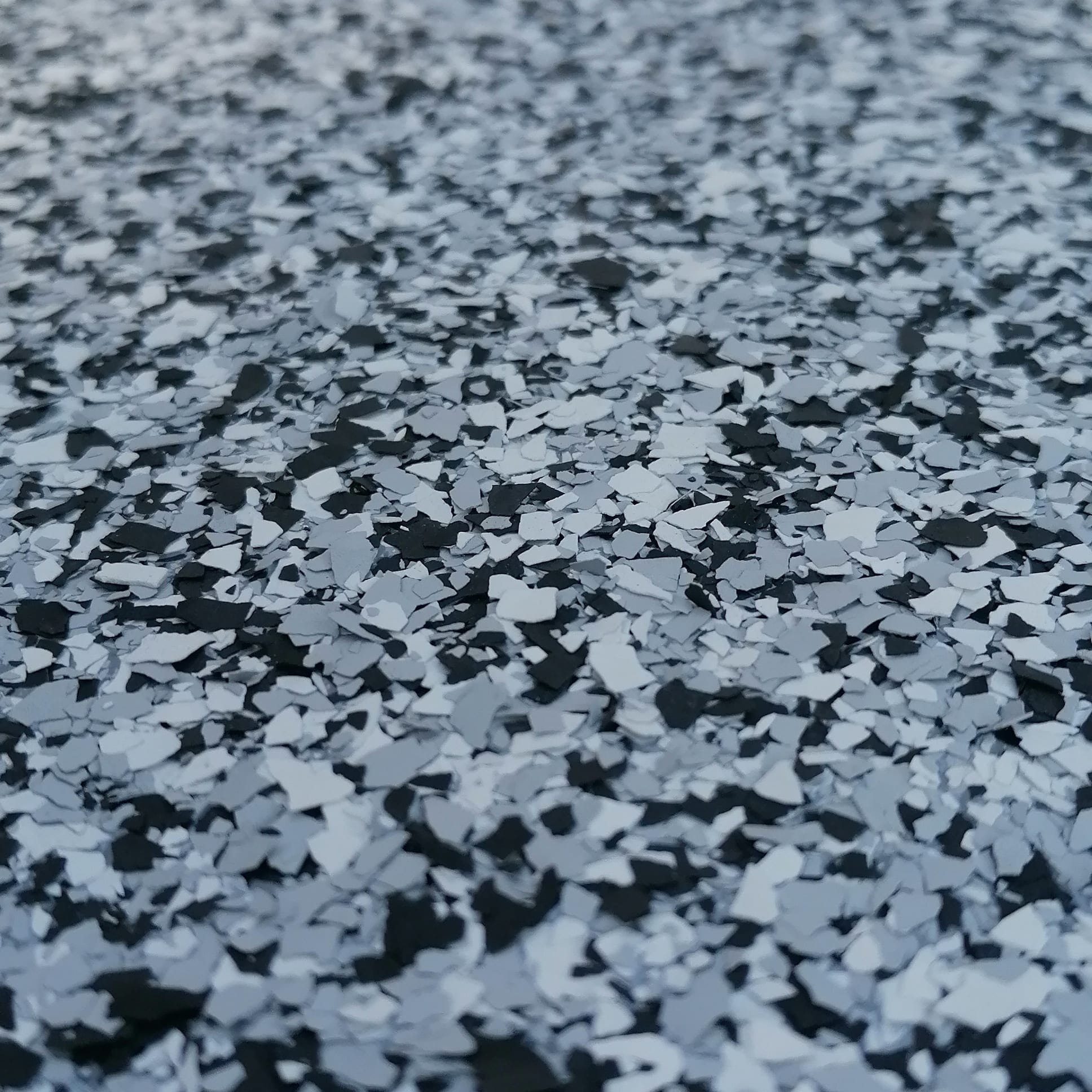 Szczegółowe ujęcie posadzki żywicznej z dekoracyjnymi płatkami w odcieniach szarości i czerni, ukazujące jej teksturę i wykończenie.