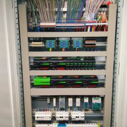 CITY CREATE BARTOSZ WANOT - Rozdzielnica elektryczna z licznymi przewodami i modułami sterującymi, zainstalowana w Pozezdrzu. Widoczne kable uporządkowane w wiązki, zasilacze impulsowe i bezpieczniki.