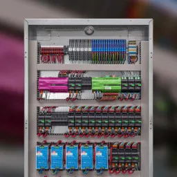 Rozdzielnica elektryczna z modułami sterującymi Loxone w kolorach różowym i zielonym, liczne przewody i złączki, widok z przodu na kompletną instalację w metalowej obudowie.