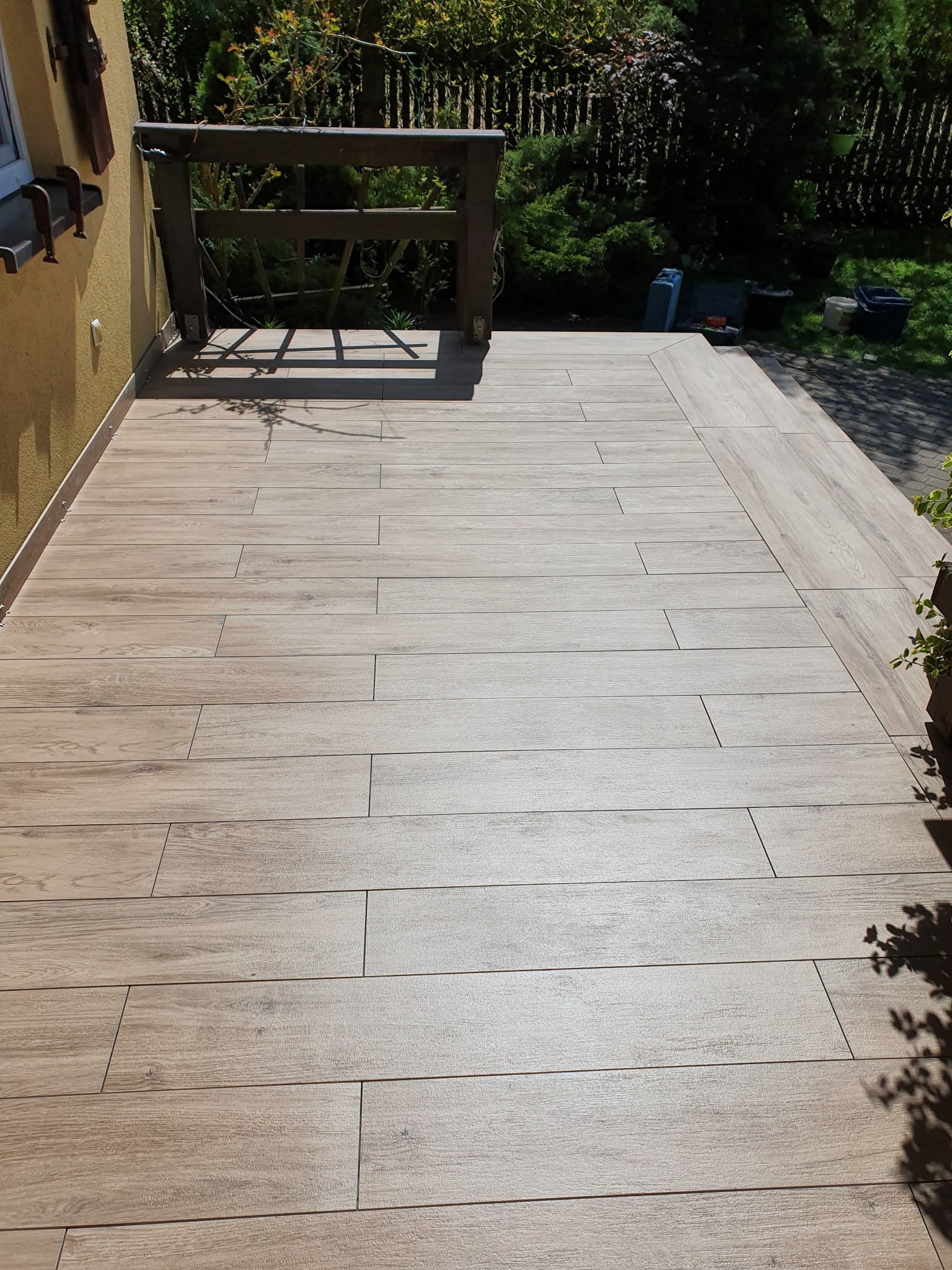 Wyłożony płytkami imitującymi drewno taras z niską balustradą, widok z góry w słoneczny dzień.