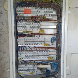 Rozdzielnica elektryczna z zamontowanymi bezpiecznikami i okablowaniem, widoczne elementy marki Hager i Simtec, zamontowana na ścianie z betonu komórkowego z widoczną pianką montażową w szczelinach.